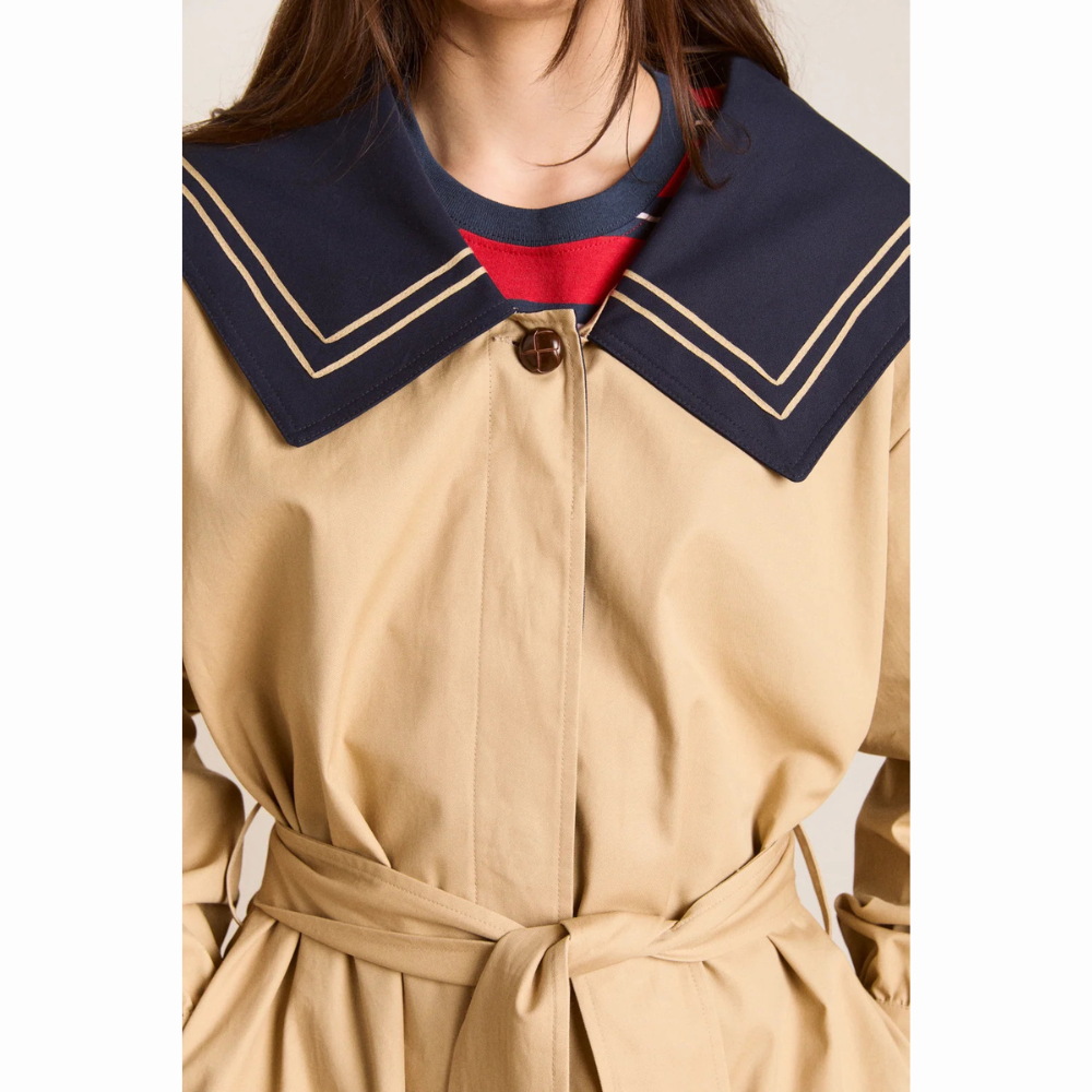 Nærbillede af den øverste del af Damson Madder Ella Trench med beige stof, brun knap og stor mørkeblå sailor-krave med dobbelte beige striber langs kanten.