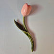 Håndlavet Odd Mud vægkunst formet som en lyserød tulipan med grøn stilk og blad på lys baggrund.
