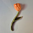 Håndlavet Odd Mud vægkunst formet som en orange tulipan med grøn stilk og blad på lys baggrund.
