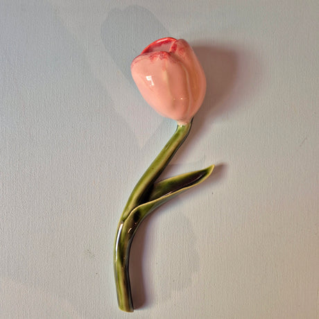 Håndlavet Odd Mud vægkunst formet som en lyserød tulipan med grøn stilk og blad på lys baggrund.