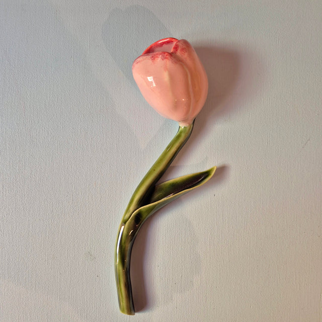 Håndlavet Odd Mud vægkunst formet som en lyserød tulipan med grøn stilk og blad på lys baggrund.