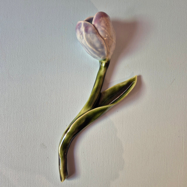 Håndlavet Odd Mud tulipan i keramik med blomst i lilla nuancer, grøn stilk og lange blade på lys baggrund.