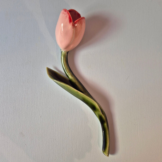 Håndlavet Odd Mud vægkunst formet som en lyserød tulipan med rødlige detaljer, grøn stilk og langt blad på lys baggrund.