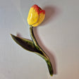 Håndlavet Odd Mud vægkunst formet som en gul tulipan med rødlige spidser, grøn stilk og stort blad på lys baggrund.