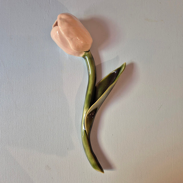 Håndlavet Odd Mud vægkunst formet som en lyserød tulipan med blank grøn stilk og enkelt blad på lys baggrund.