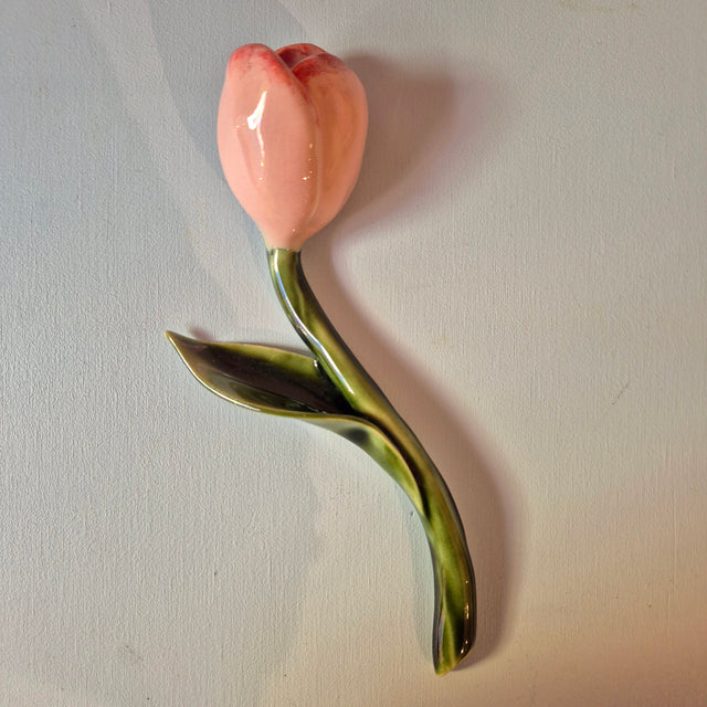 Håndlavet Odd Mud vægkunst formet som en lyserød tulipan med buet grøn stilk og blad på lys baggrund.