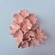 Håndlavet Odd Mud vægkunst i blank lyserød keramik med en tæt samling af skulpturelle blomster set forfra.
