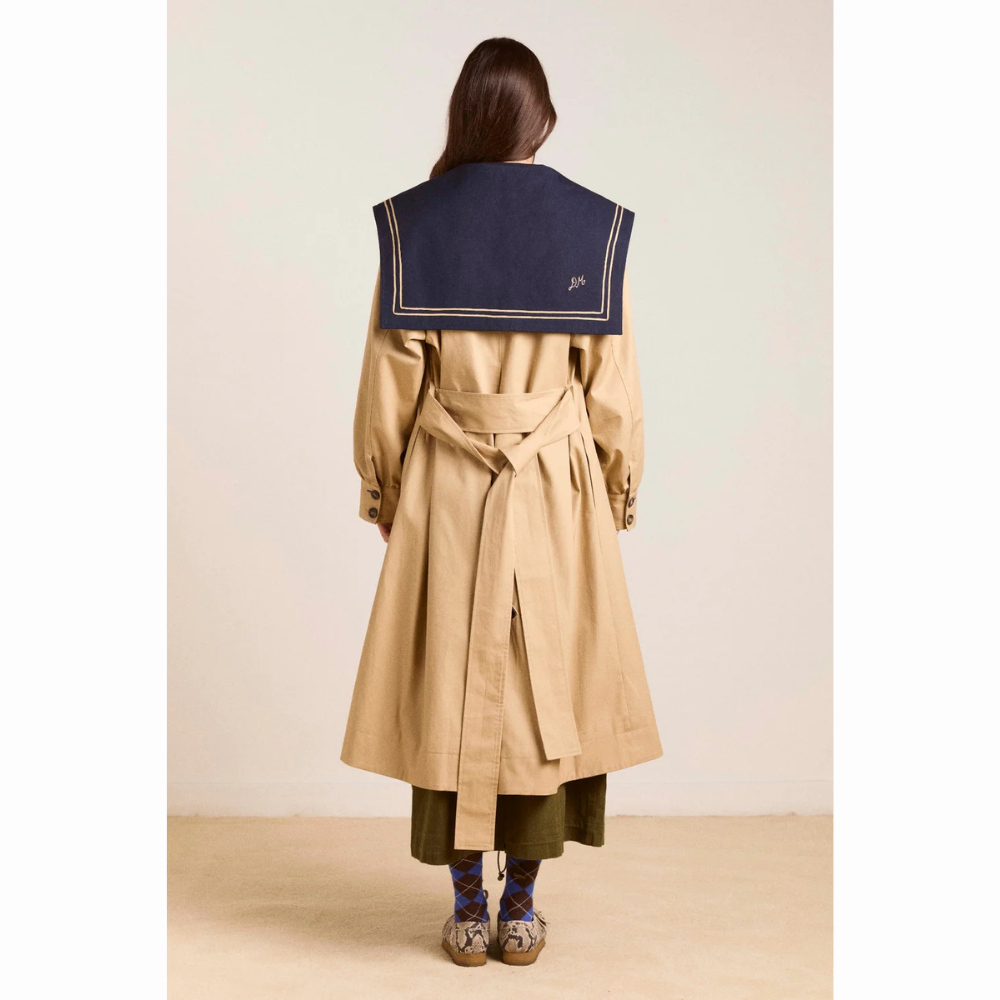 Damson Madder Ella Trench set bagfra. Den beige trenchcoat har langt snit, bindebælte i taljen og en stor mørkeblå sailor-krave, der dækker den øverste del af ryggen.