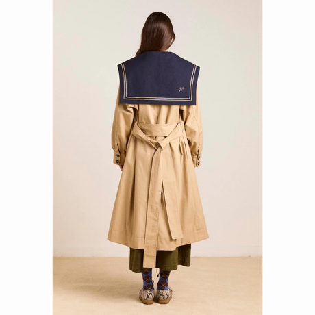 Damson Madder Ella Trench set bagfra. Den beige trenchcoat har langt snit, bindebælte i taljen og en stor mørkeblå sailor-krave, der dækker den øverste del af ryggen.