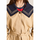 Nærbillede af den øverste del af Damson Madder Ella Trench med beige stof, brun knap og stor mørkeblå sailor-krave med dobbelte beige striber langs kanten.