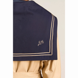 Nærbillede af bagsiden af den mørkeblå sailor-krave på Damson Madder Ella Trench. Kraven har dobbelte beige kantstriber og et lille broderet DM-logo i det ene hjørne.